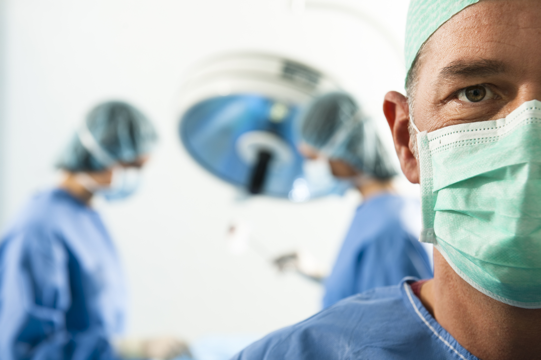 Портрет врача на фоне операционной, в которой идет операция