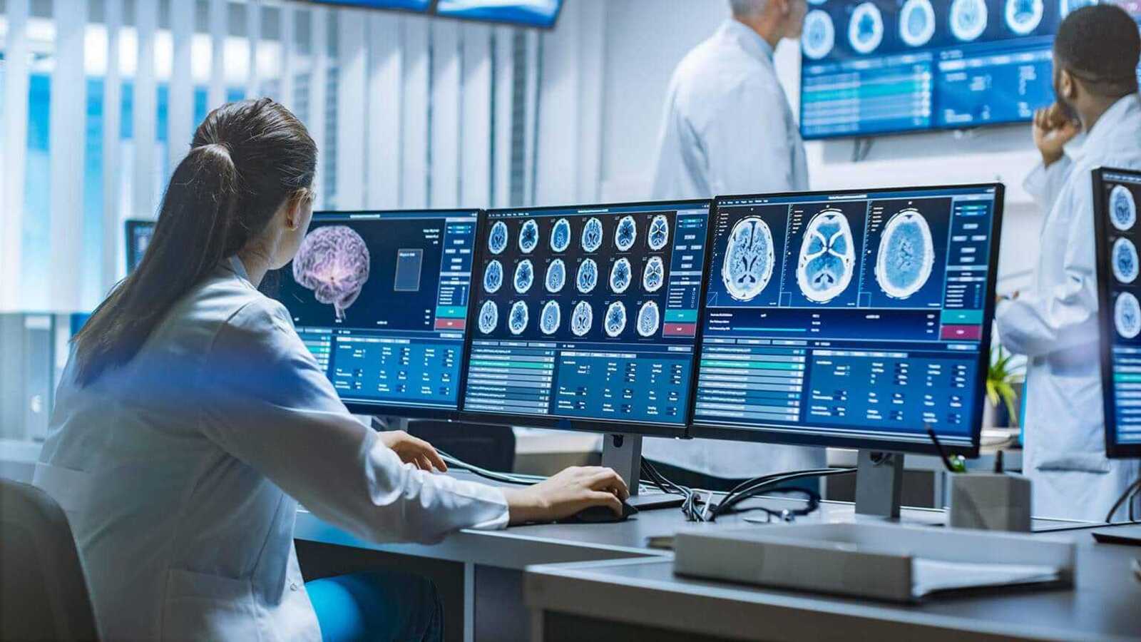 Девушка в белом халате смотрит на мониторы со снимками МРТ мозга